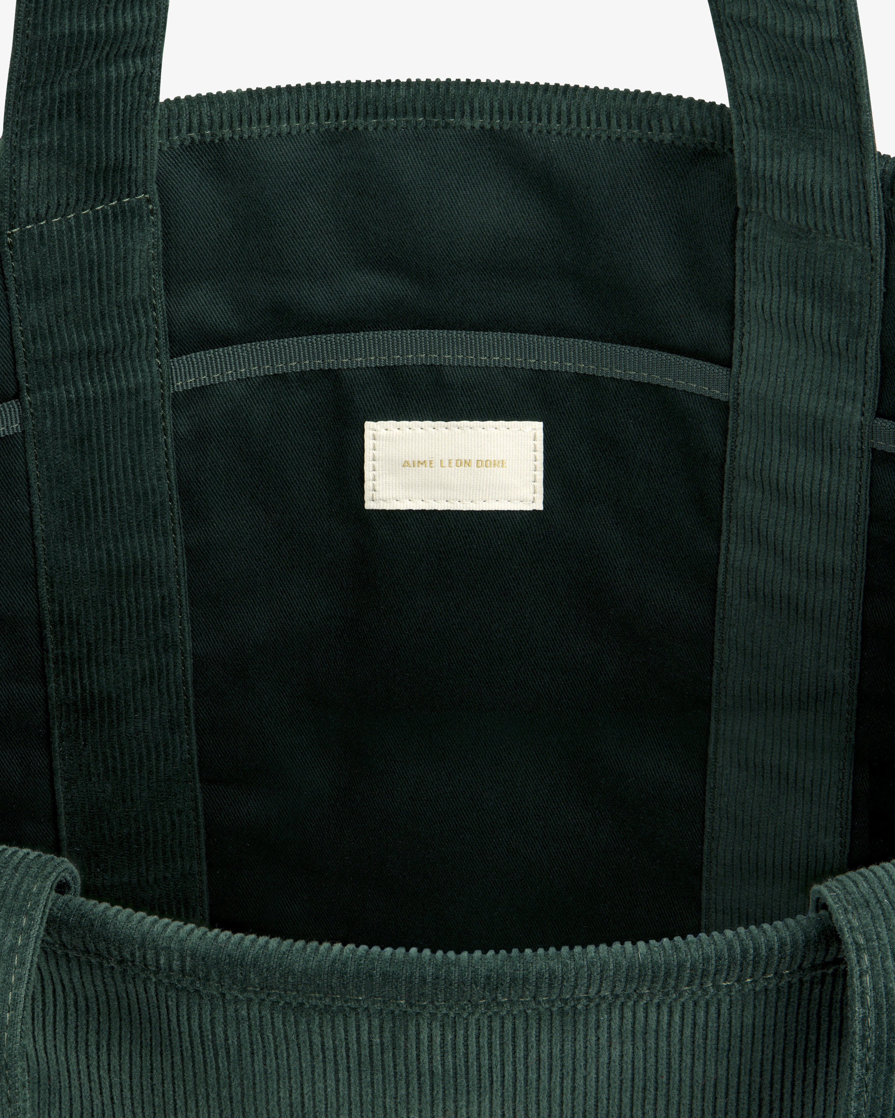Interior of a dark green Large Corduroy Unisphere Tote Bag with a centered off-white fabric label.
