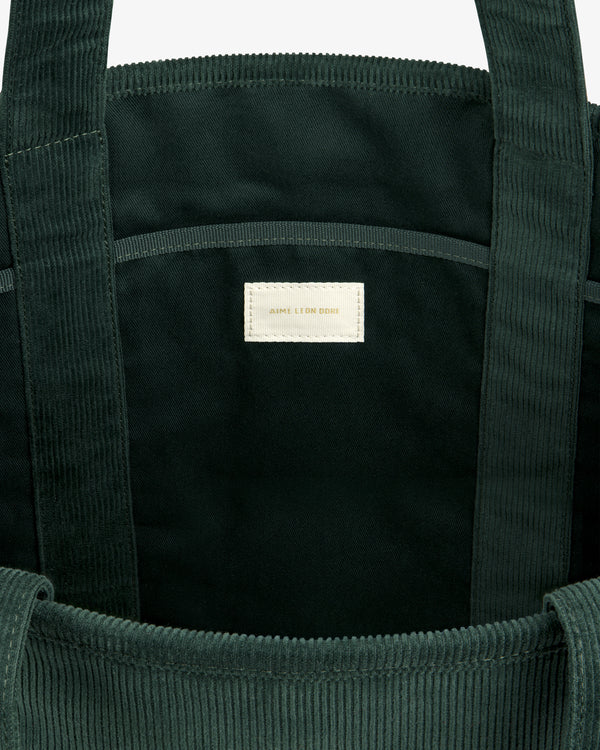 Interior of a dark green Large Corduroy Unisphere Tote Bag with a centered off-white fabric label.