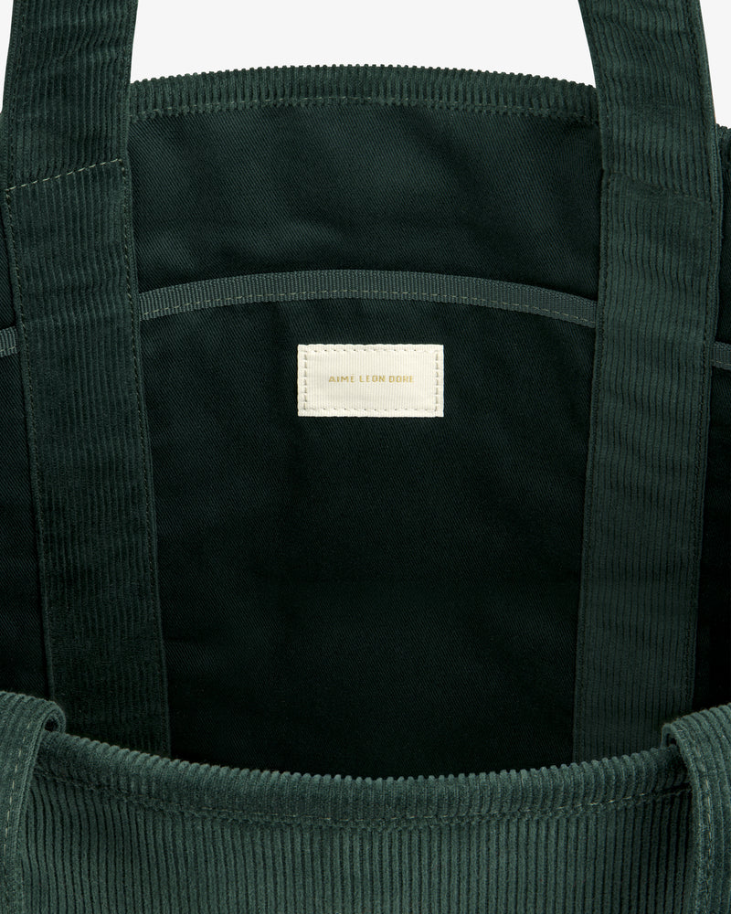 Interior of a dark green Large Corduroy Unisphere Tote Bag with a centered off-white fabric label.