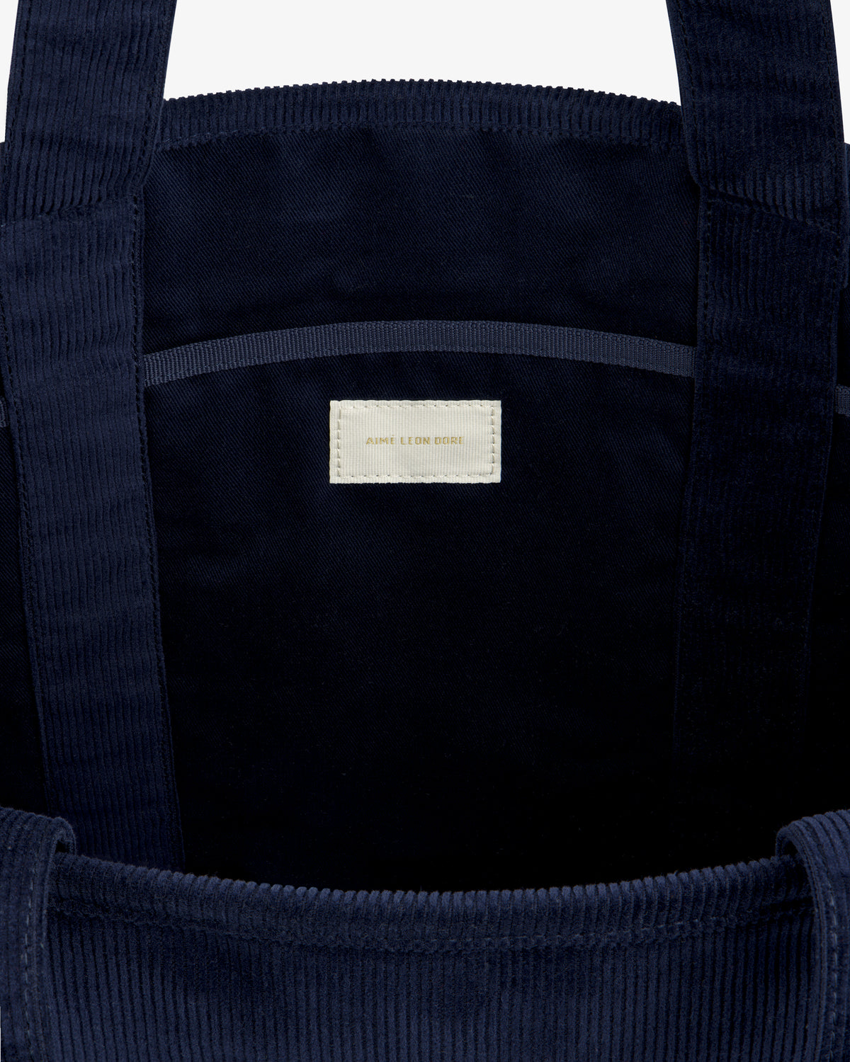 Interior of a dark blue Large Corduroy Unisphere Tote Bag featuring a central fabric label with text.