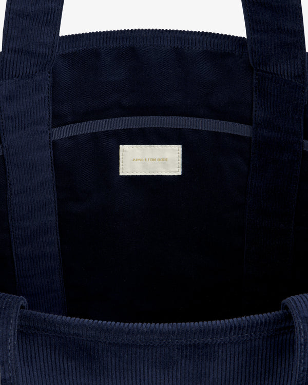 Interior of a dark blue Large Corduroy Unisphere Tote Bag featuring a central fabric label with text.