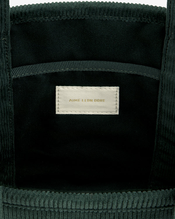 Interior of a dark green Mini Corduroy Unisphere Tote Bag featuring a central fabric label with AIME LEON DORE text.