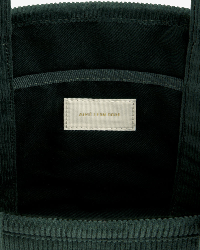 Interior of a dark green Mini Corduroy Unisphere Tote Bag featuring a central fabric label with AIME LEON DORE text.