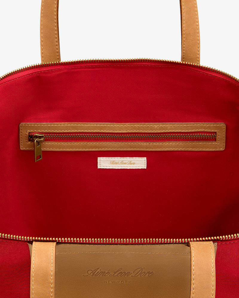 Open Leather Canvas Zip Tote in tan, revealing red lining, zippered pocket, and label stitched below the zipper.