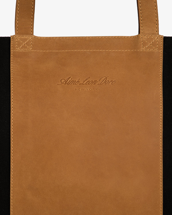 Leather Canvas Zip Tote with Aimé Leon Dore New York embossing and sturdy handles, made of brown leather.