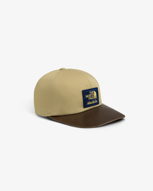 ALD / The North Face Leather Brim Logo Hat: beige cap, brown leather brim, blue & yellow front patch.