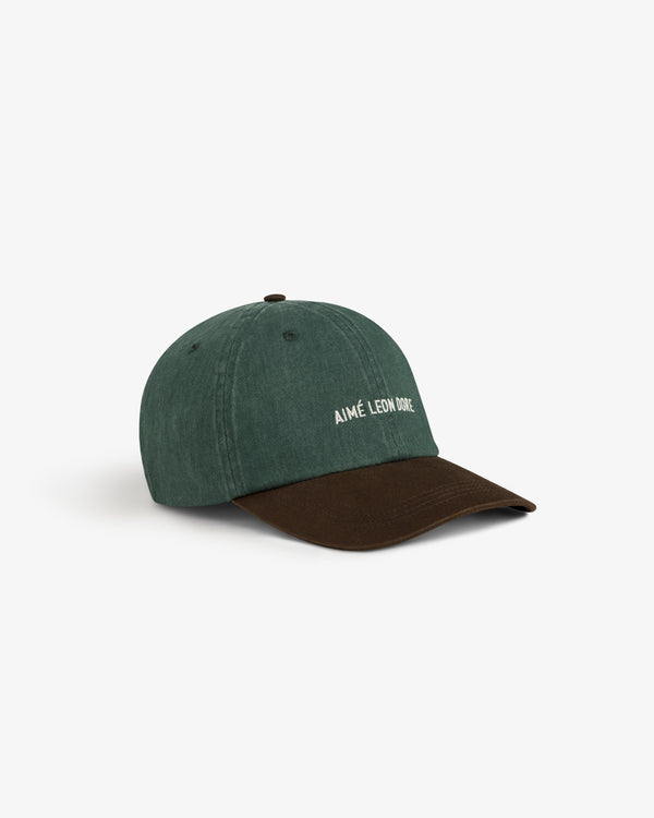 Pigment Dyed Logo Hat: green cap, brown brim, white AIMÉ LEON DORE text on front, shown on white background.