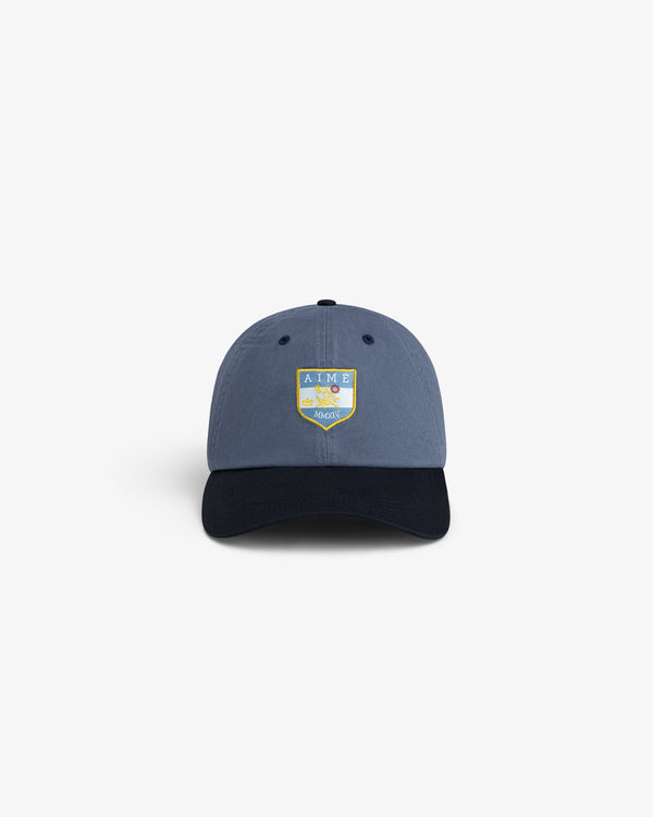 Crest Shield Hat: Blue cap with black brim, yellow-blue AIME LEON DORE HARVEST shield logo on the front.