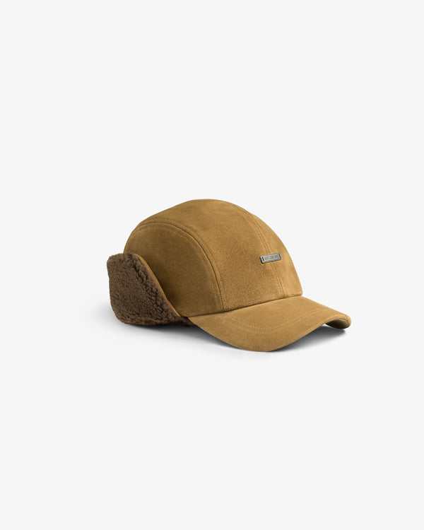 Tan Shearling Earflap Hat with fold-down fuzzy earflaps and a small rectangular logo plaque.