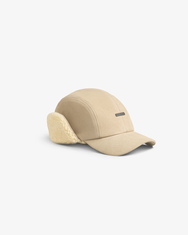 Beige Shearling Earflap Hat with fold-down fleece earflaps and a small metal logo plaque.