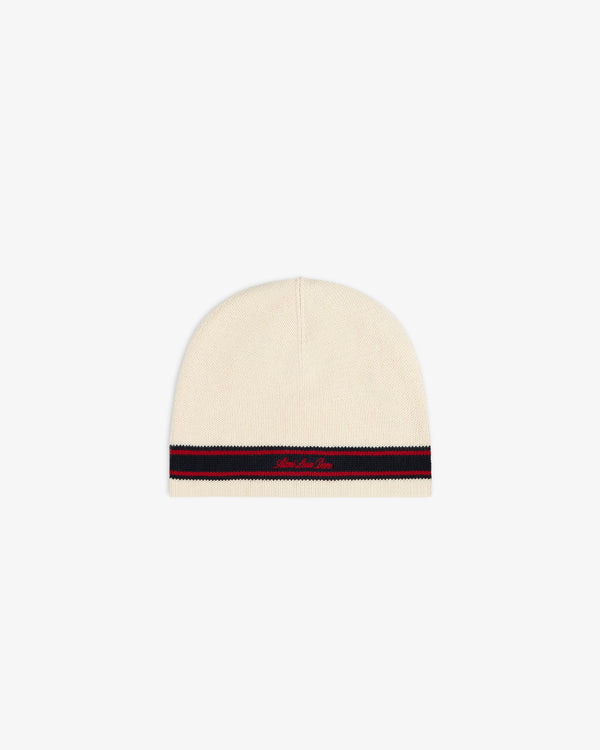 Stripe Knit Beanie in beige with red/navy stripes near the edge and red cursive text above the stripes.