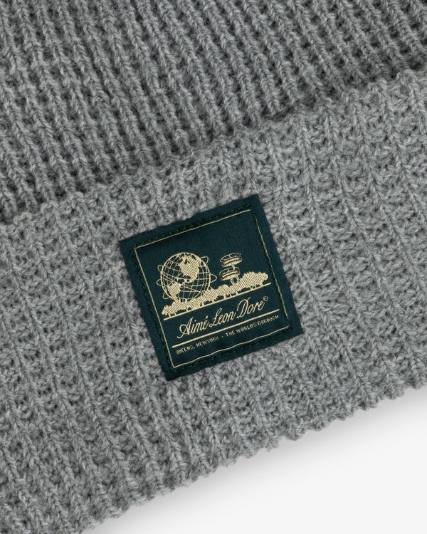 Close-up of a gray Waffle Knit Beanie with a patch showing a globe, books, and Aimé Leon Dore text.
