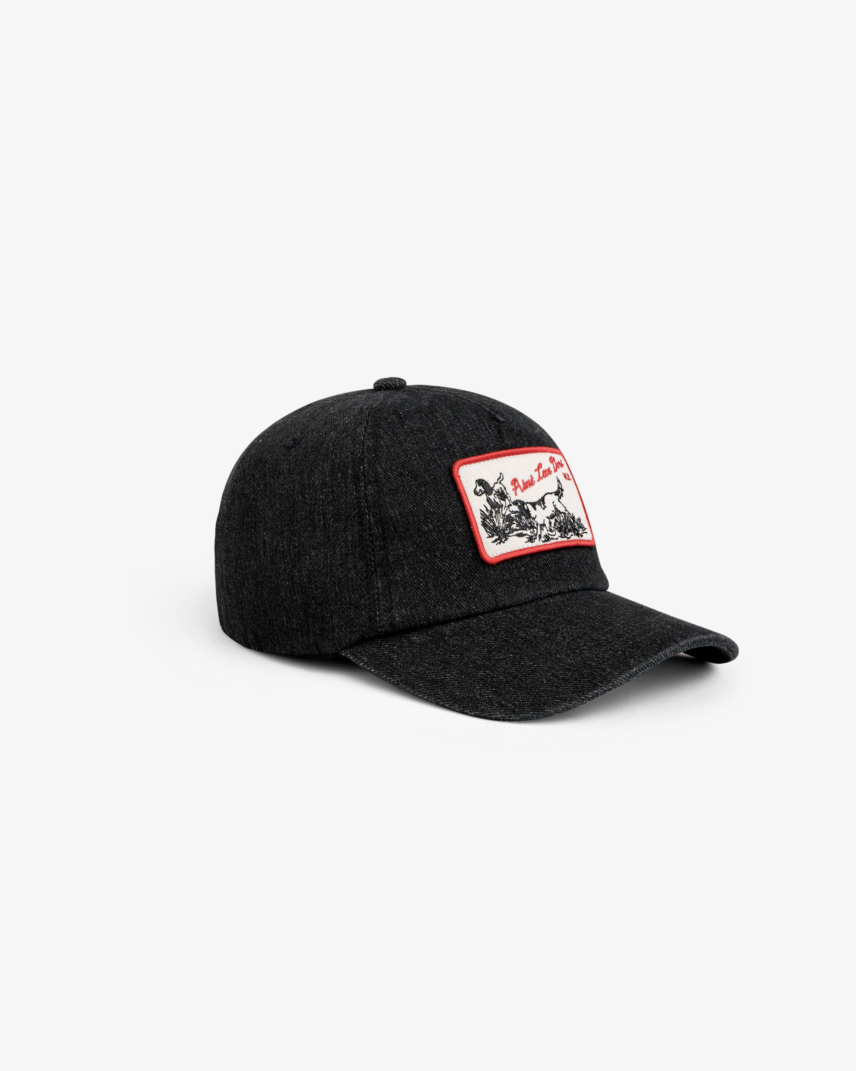 Aimé Retriever Hat: a black baseball cap with a rectangular patch featuring a dog illustration and red trim.