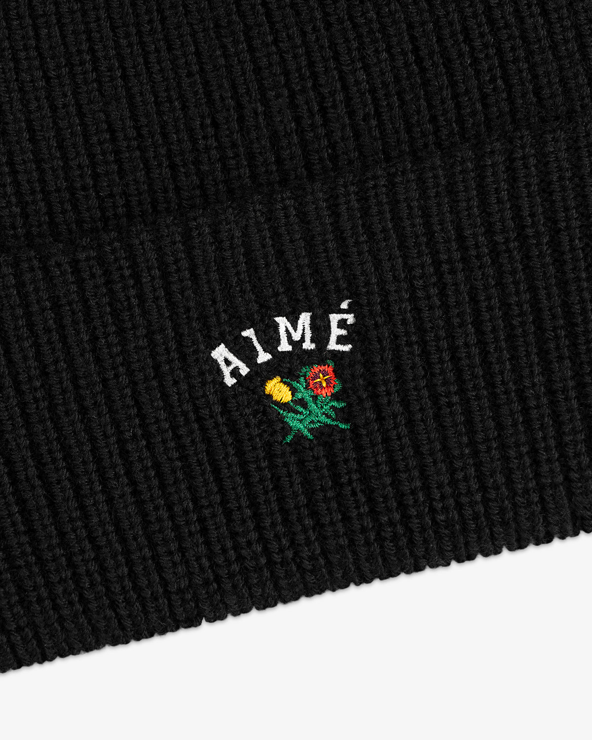 Crest Merino Wool Beanie in black with AIMÉ and embroidered yellow and red flowers below the text.