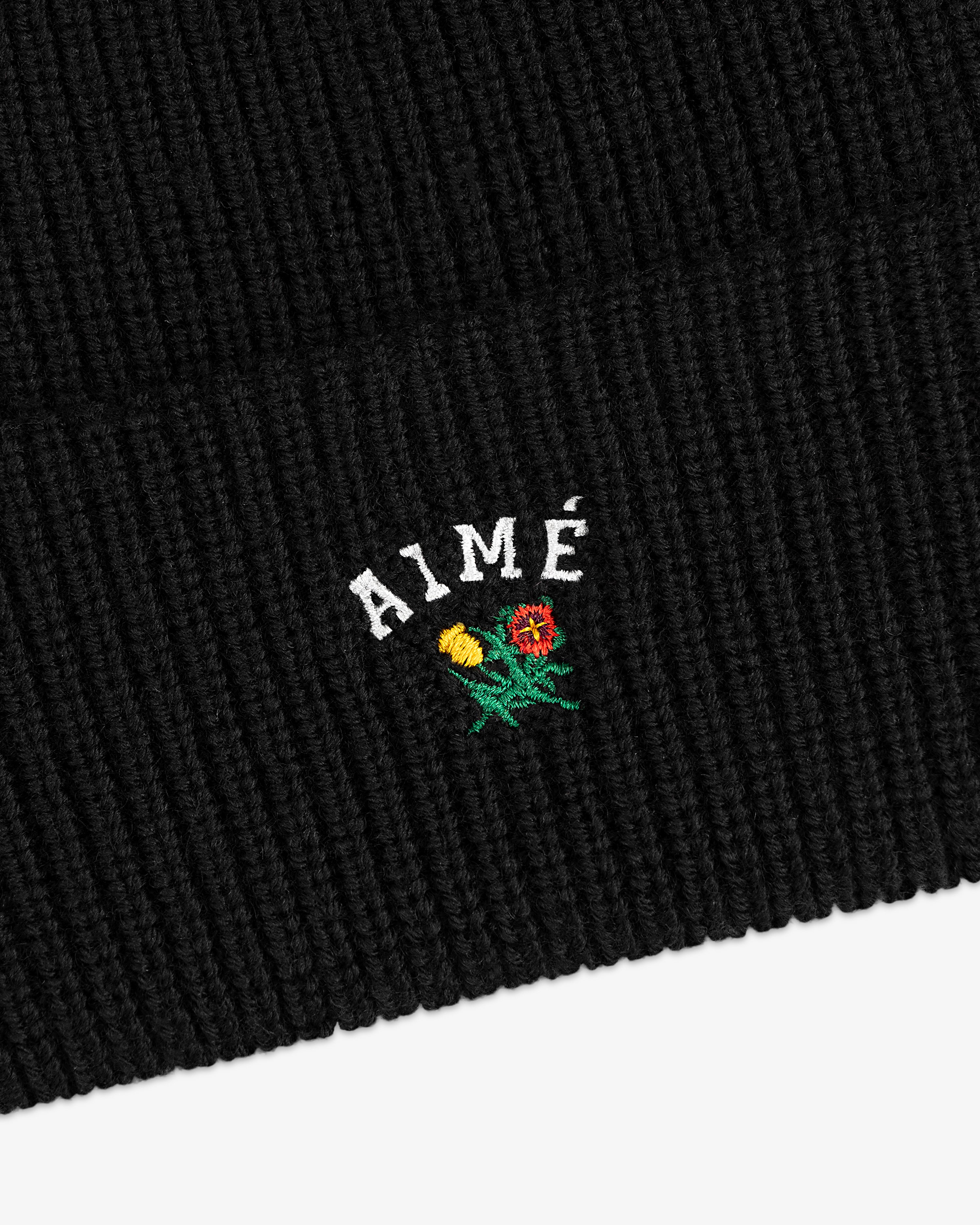 Crest Merino Wool Beanie in black with AIMÉ and embroidered yellow and red flowers below the text.