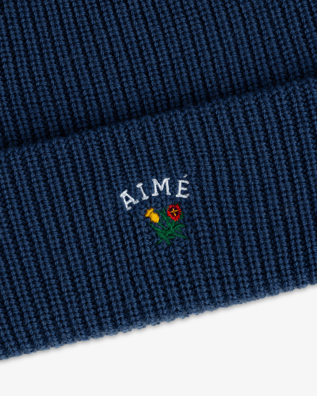 Blue Crest Merino Wool Beanie with AIME and a small yellow/red flower embroidered on the fold.