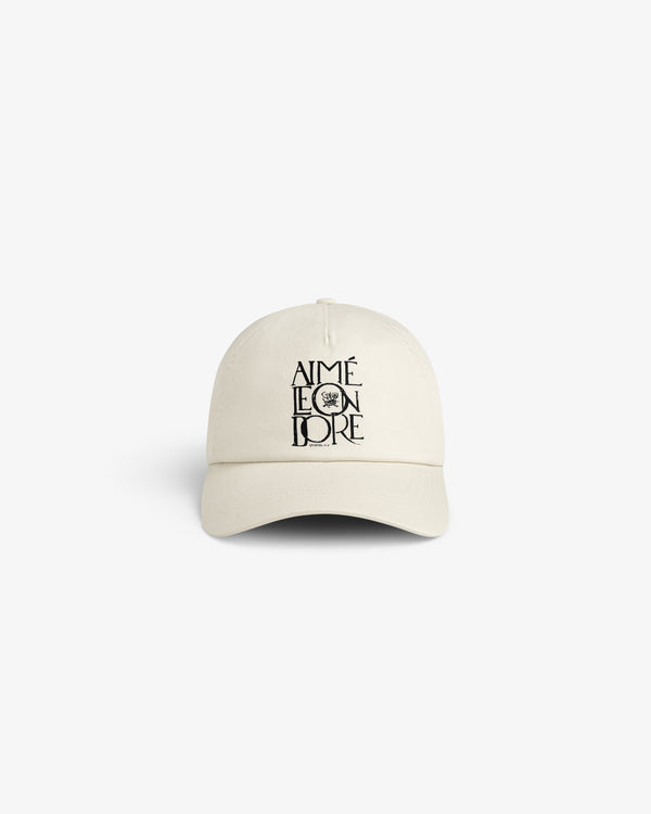 A beige Stacked Logo Hat with AIMÉ LEON DORE and a small black graphic printed on the front.