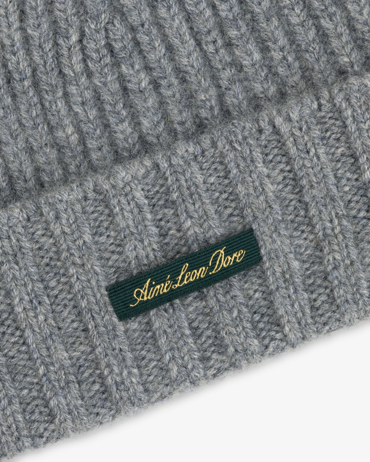 Close-up of a grey ribbed Cashmere Beanie with a green woven label featuring gold embroidered text.