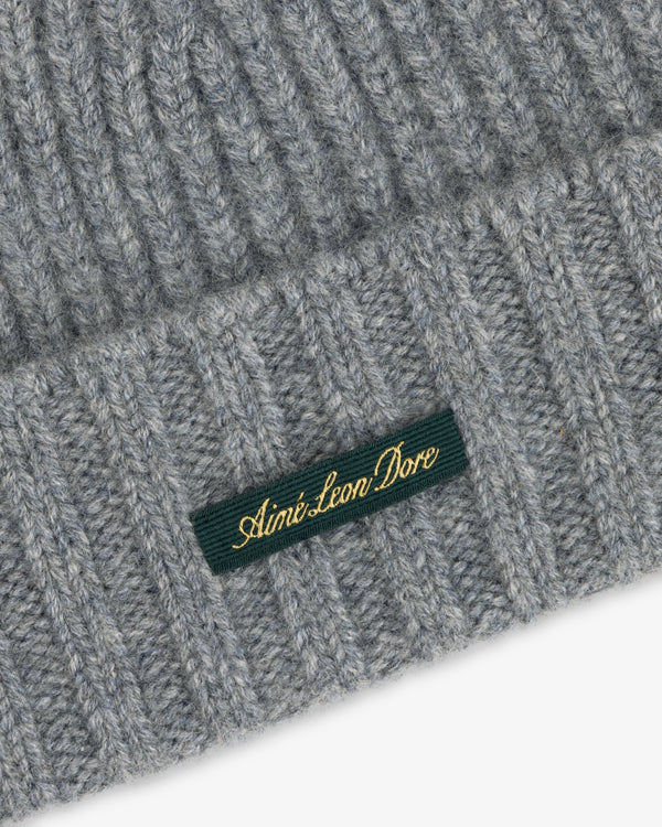 Close-up of a grey ribbed Cashmere Beanie with a green woven label featuring gold embroidered text.