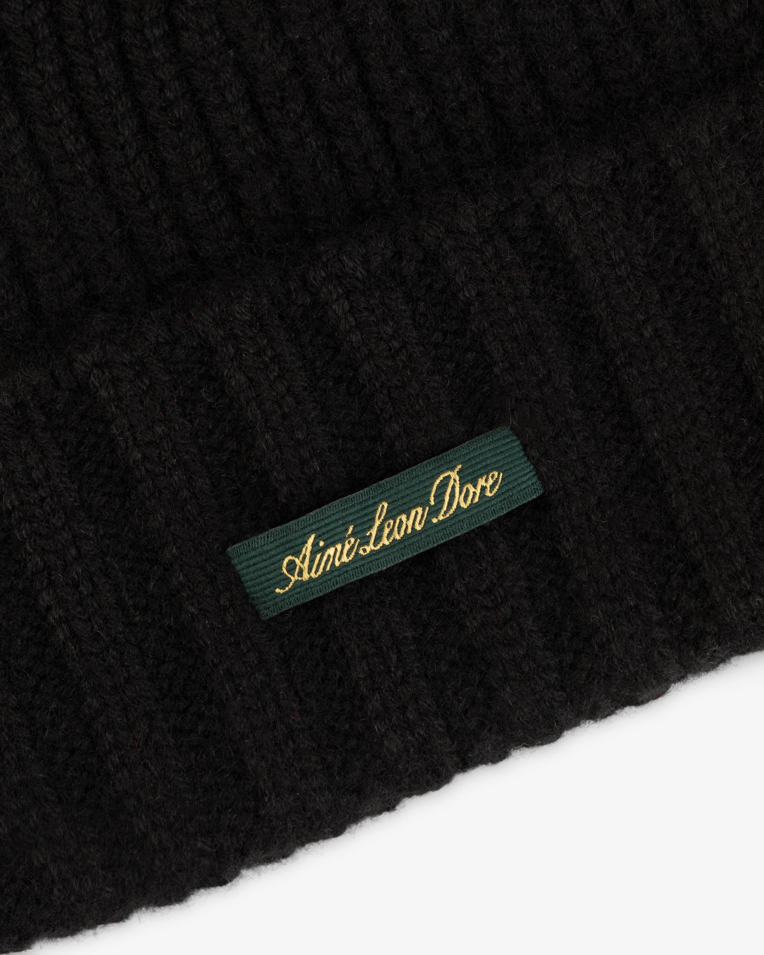 Black ribbed knit Cashmere Beanie featuring a rectangular green label with gold embroidered text.