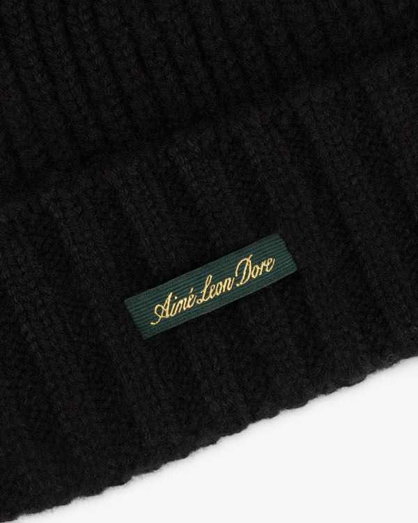 Black ribbed knit Cashmere Beanie featuring a rectangular green label with gold embroidered text.