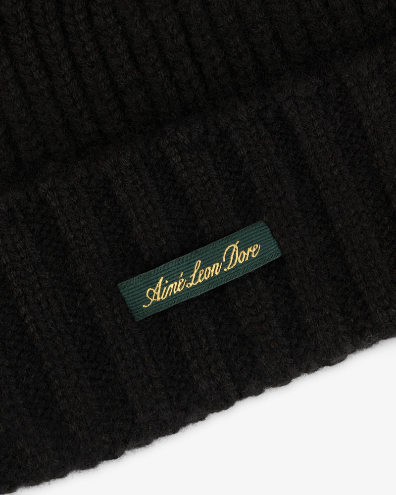 Black ribbed knit Cashmere Beanie featuring a rectangular green label with gold embroidered text.