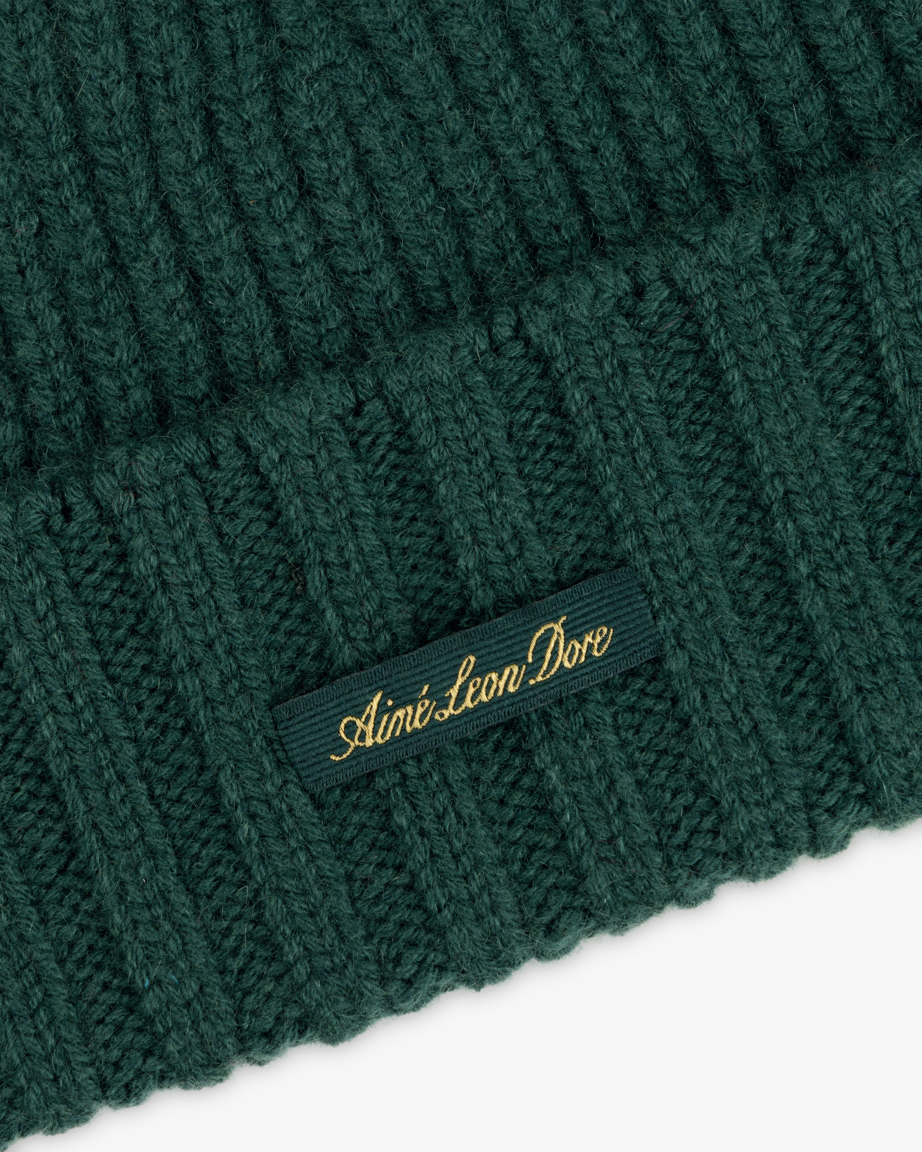 Close-up of a ribbed dark green Cashmere Beanie with a small tag featuring gold text.