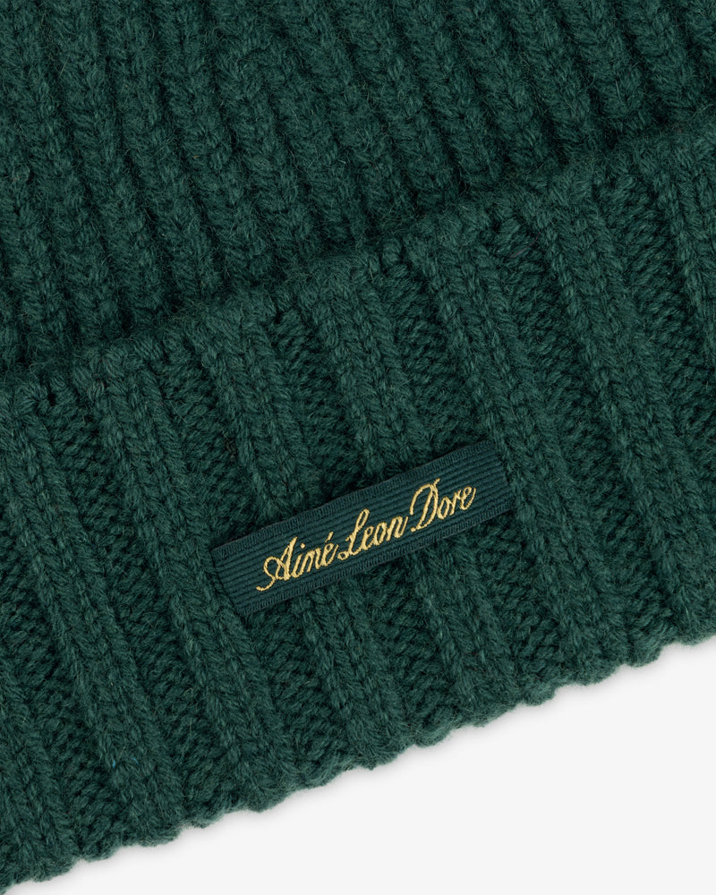 Close-up of a ribbed dark green Cashmere Beanie with a small tag featuring gold text.