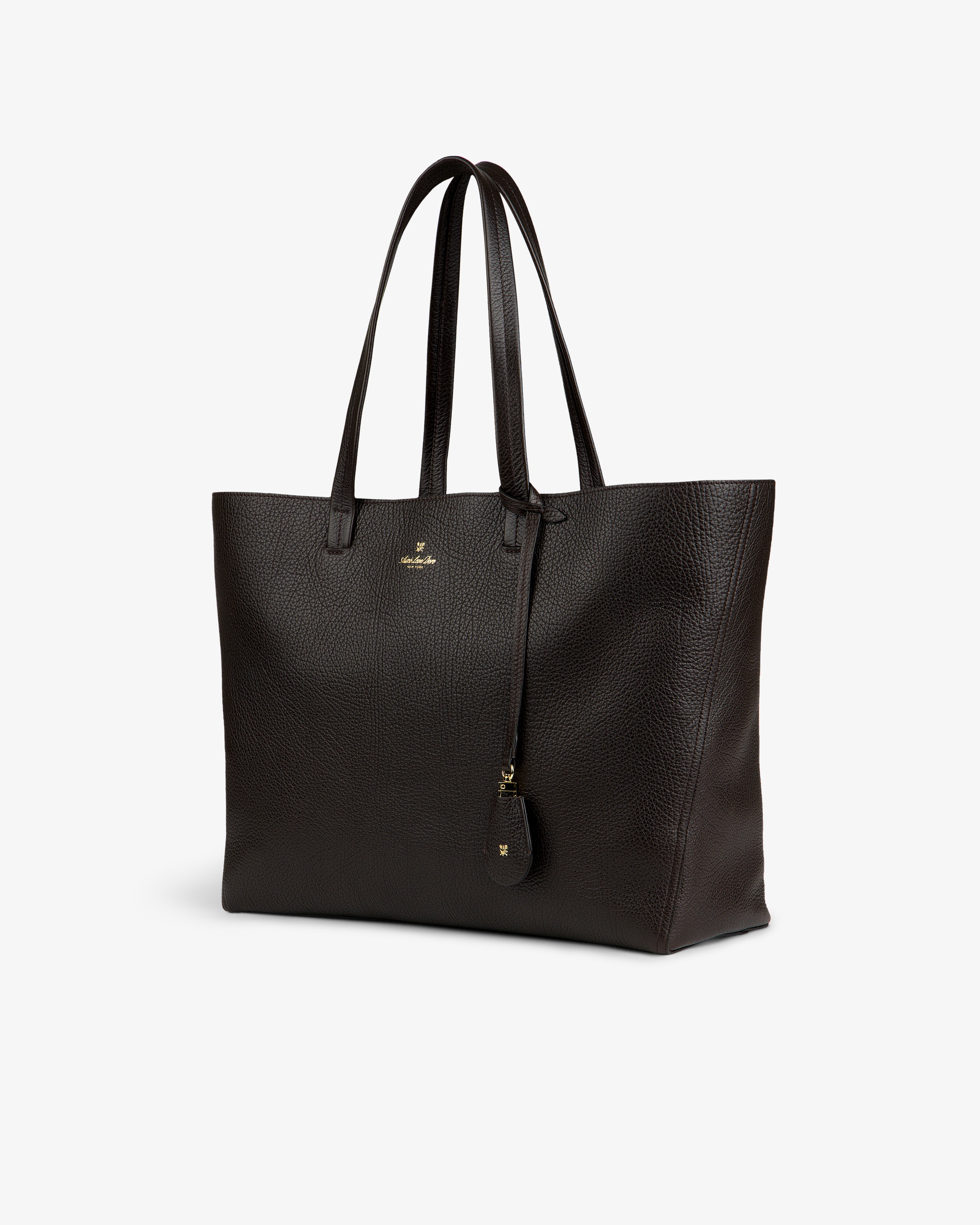 Tumbled Leather Tote Bag in dark brown with double handles, gold logo, and keychain on white background.