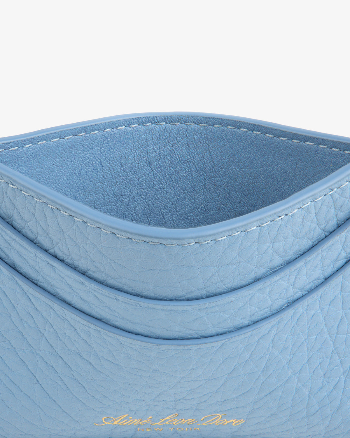 Close-up of the Tumbled Leather Card Holder in light blue with curved edges and gold embossed text at the bottom.
