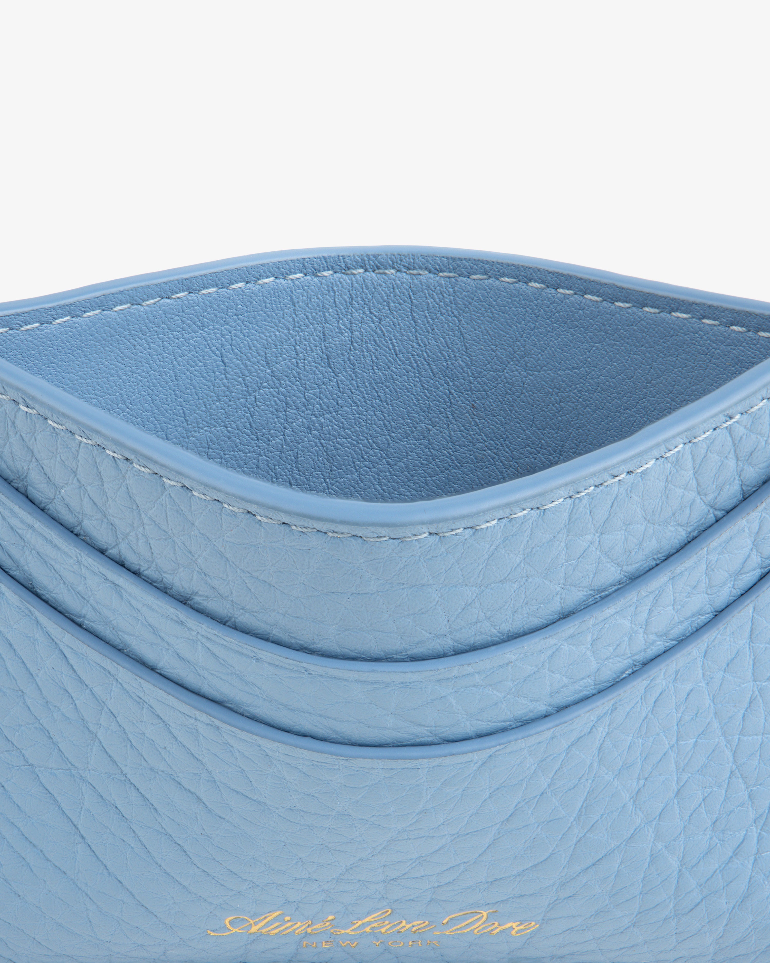 Close-up of the Tumbled Leather Card Holder in light blue with curved edges and gold embossed text at the bottom.