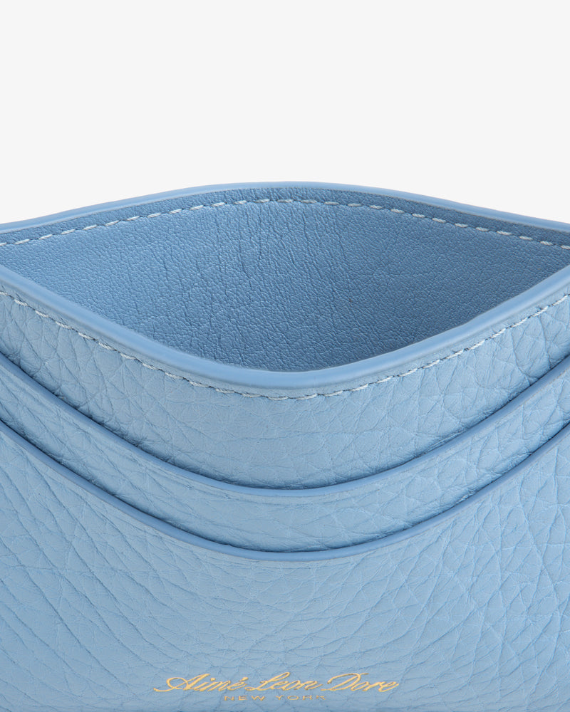 Close-up of the Tumbled Leather Card Holder in light blue with curved edges and gold embossed text at the bottom.