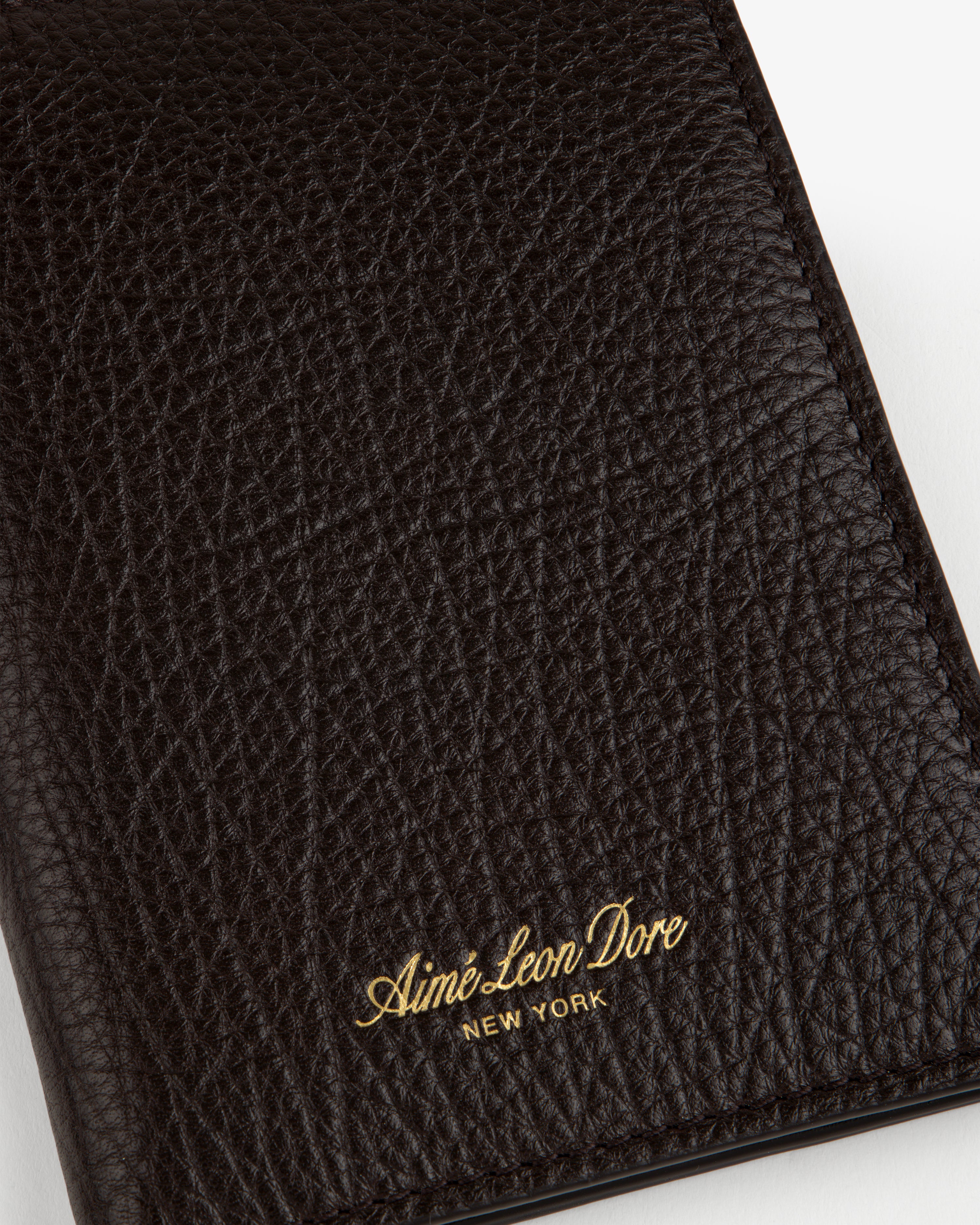 Close-up of a textured black Tumbled Leather Passport Holder with Aimé Leon Dore NEW YORK in gold lettering.