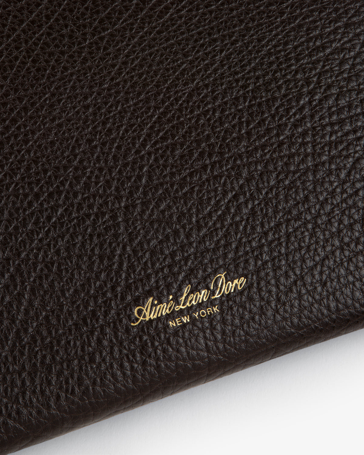 Close-up of Small Tumbled Leather Pouch’s black textured leather, embossed with gold Aimé Leon Dore NEW YORK.