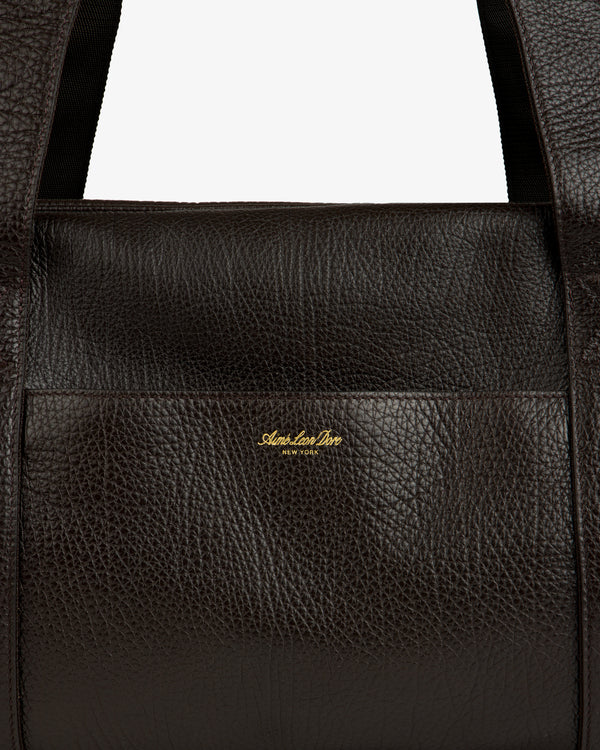 Close-up of the Tumbled Leather Duffle in dark brown with gold Aimé Leon Dore NEW YORK logo on the front.
