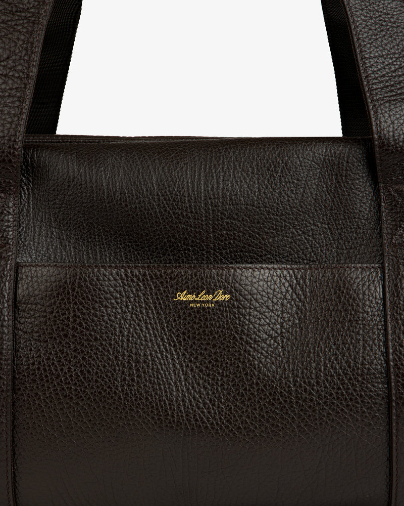 Close-up of the Tumbled Leather Duffle in dark brown with gold Aimé Leon Dore NEW YORK logo on the front.
