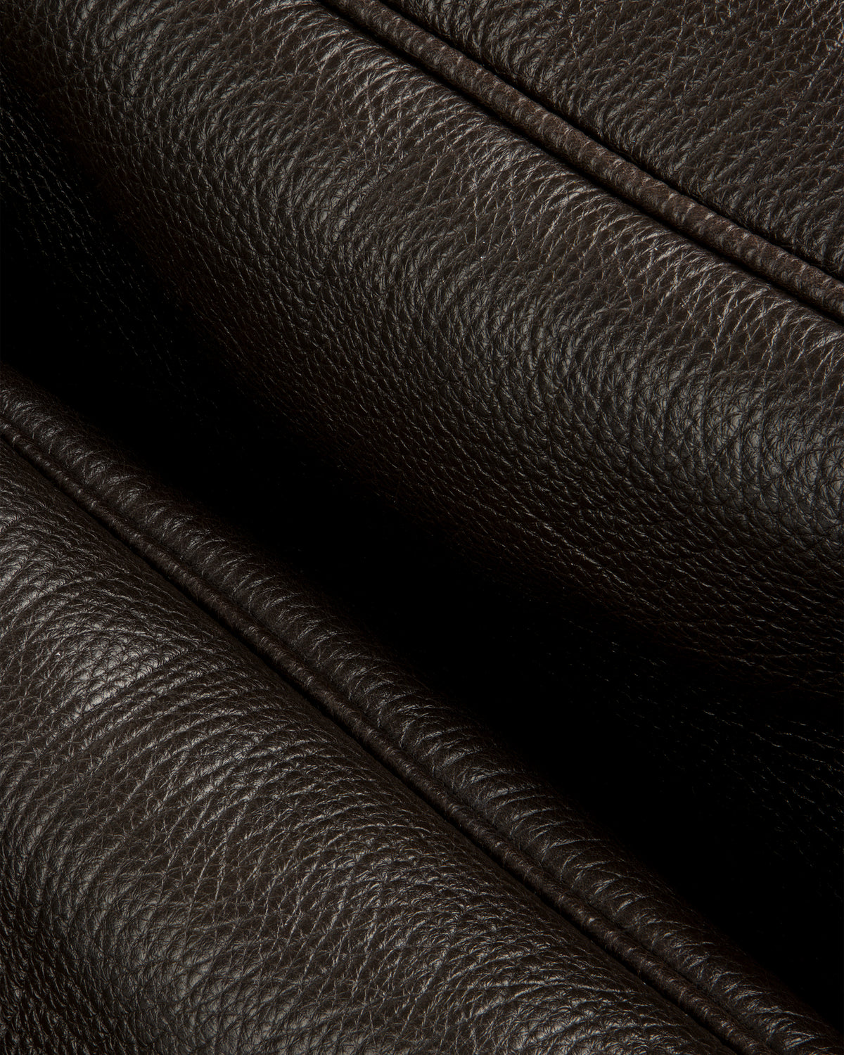 Close-up of Tumbled Leather Duffle’s dark brown textured leather with visible grain and stitched folded edges.