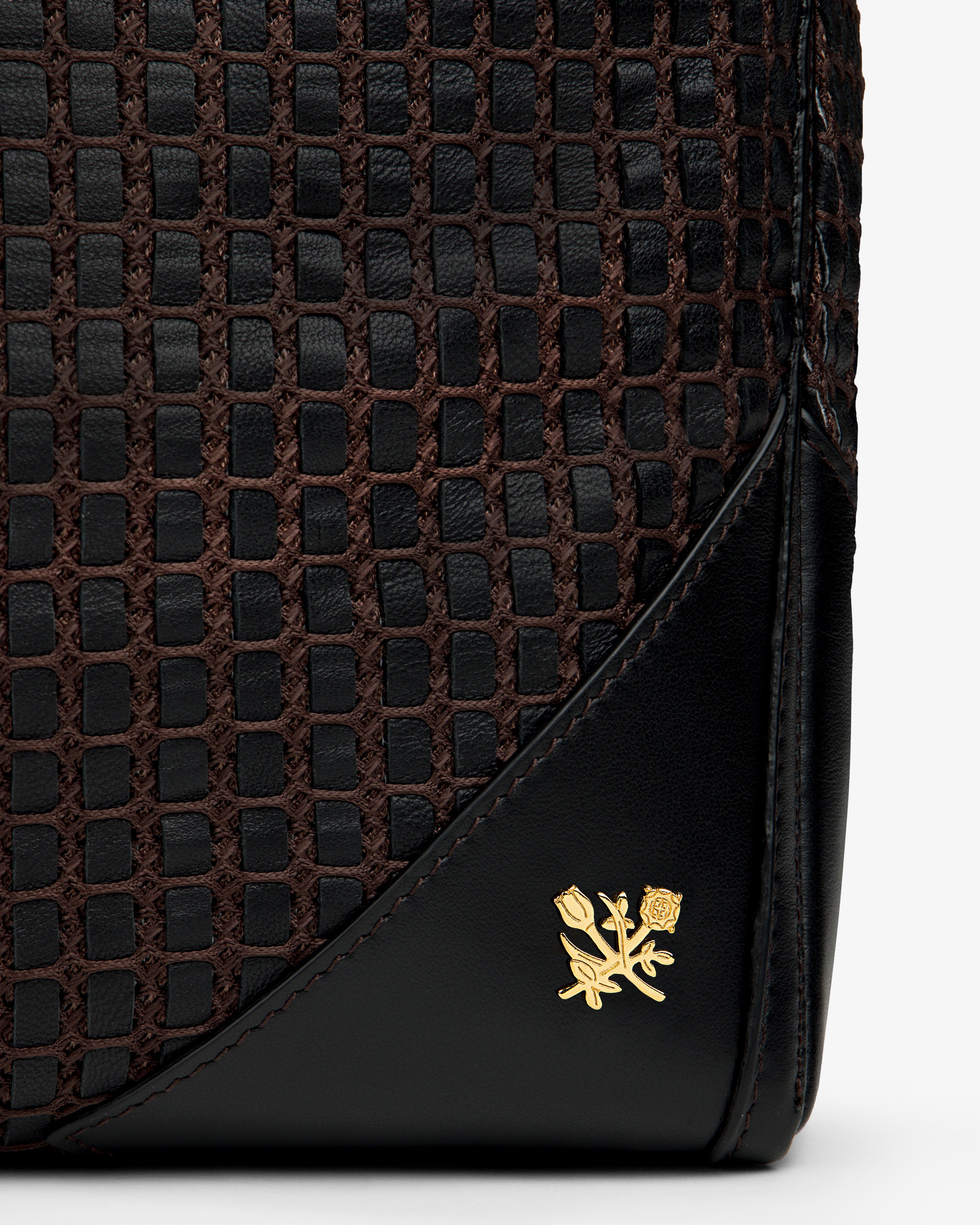 Close-up of a black and brown Woven Leather Tote Bag with a gold floral emblem.