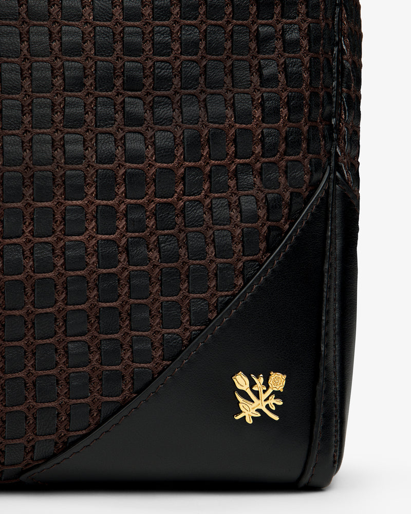 Close-up of a black and brown Woven Leather Tote Bag with a gold floral emblem.