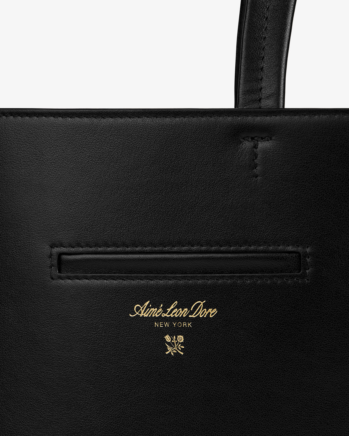 Close-up of a black Napa Leather Shoulder Bag with a gold embossed logo and a floral emblem.