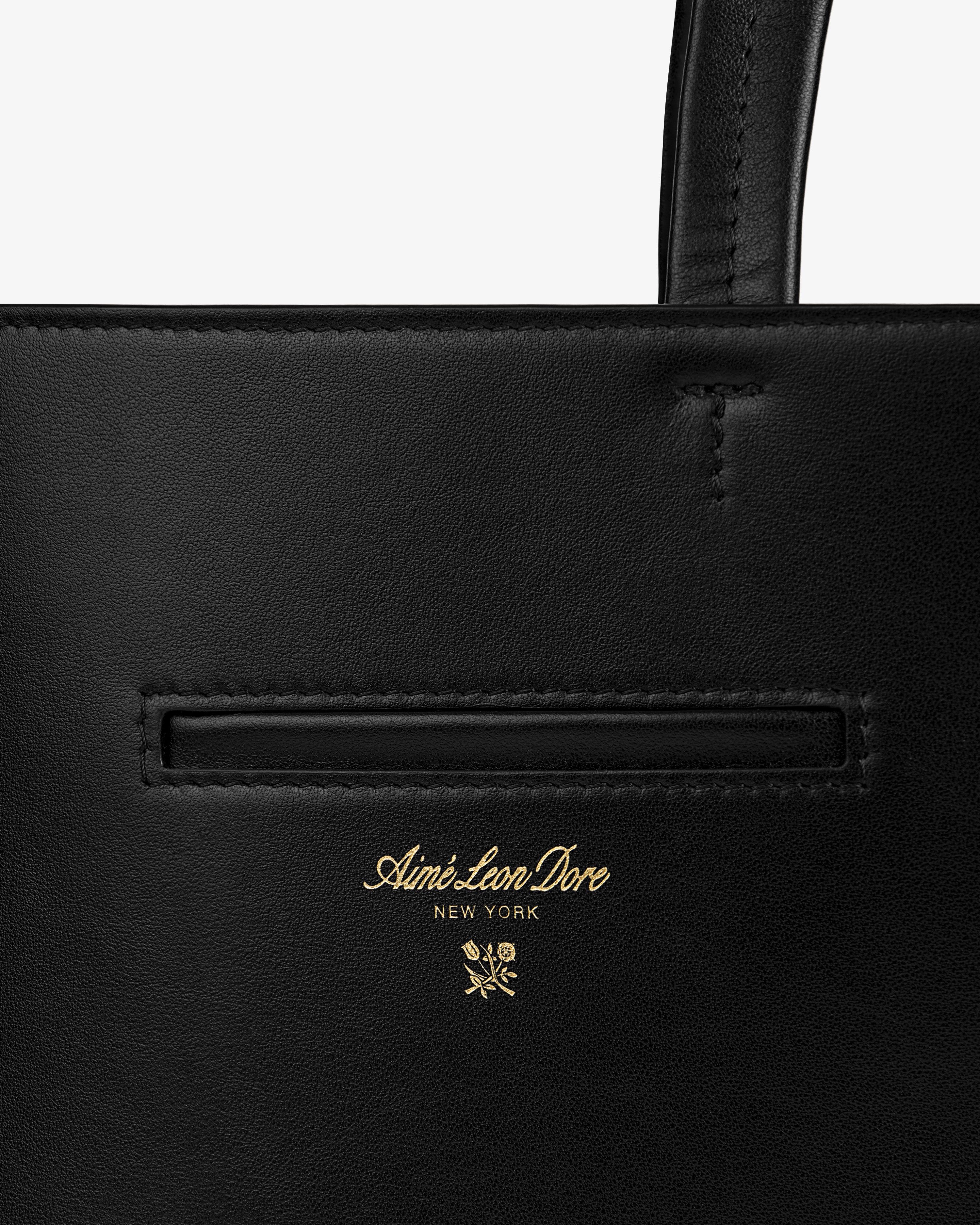 Close-up of a black Napa Leather Shoulder Bag with a gold embossed logo and a floral emblem.