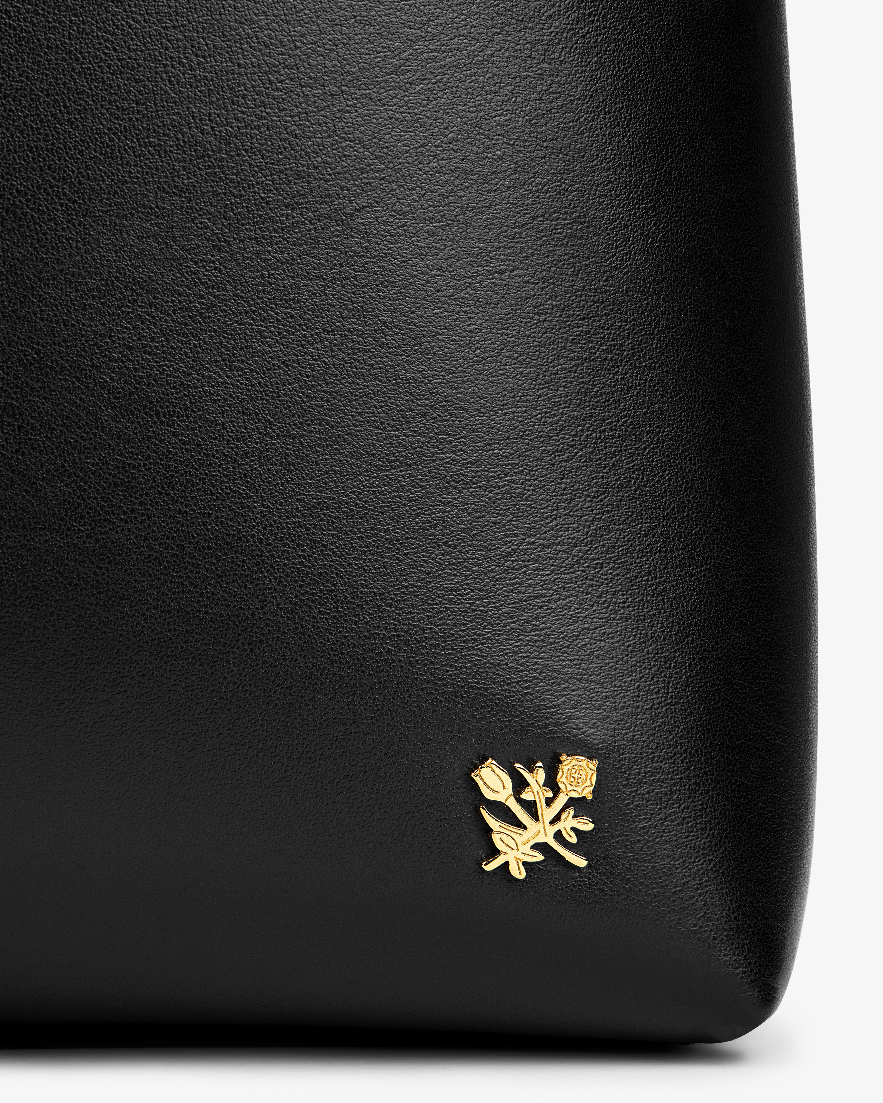 Napa Leather Shoulder Bag in black featuring a small gold floral emblem in the corner.