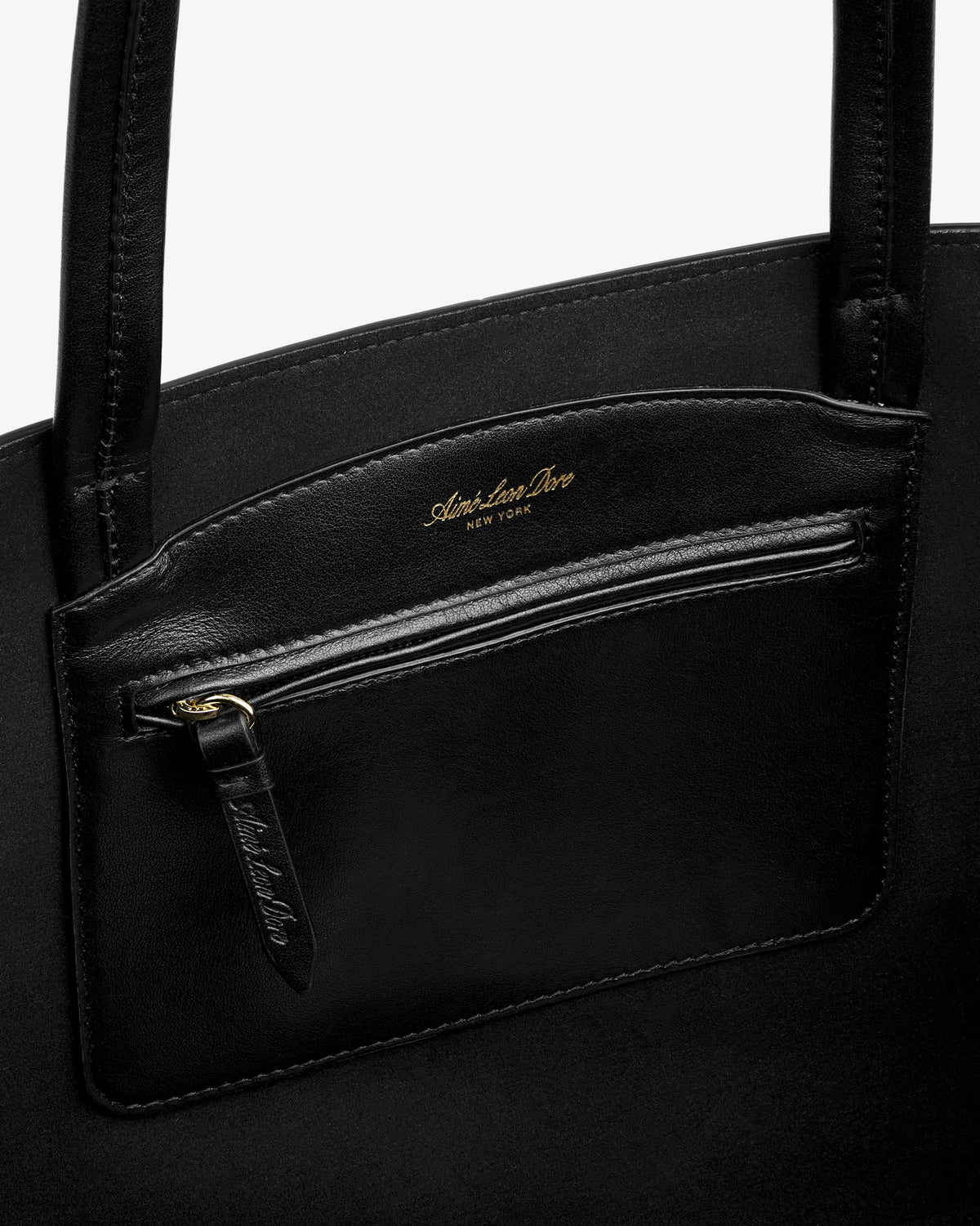 Interior of a black leather Napa Leather Shoulder Bag with a zippered pocket featuring gold lettering.