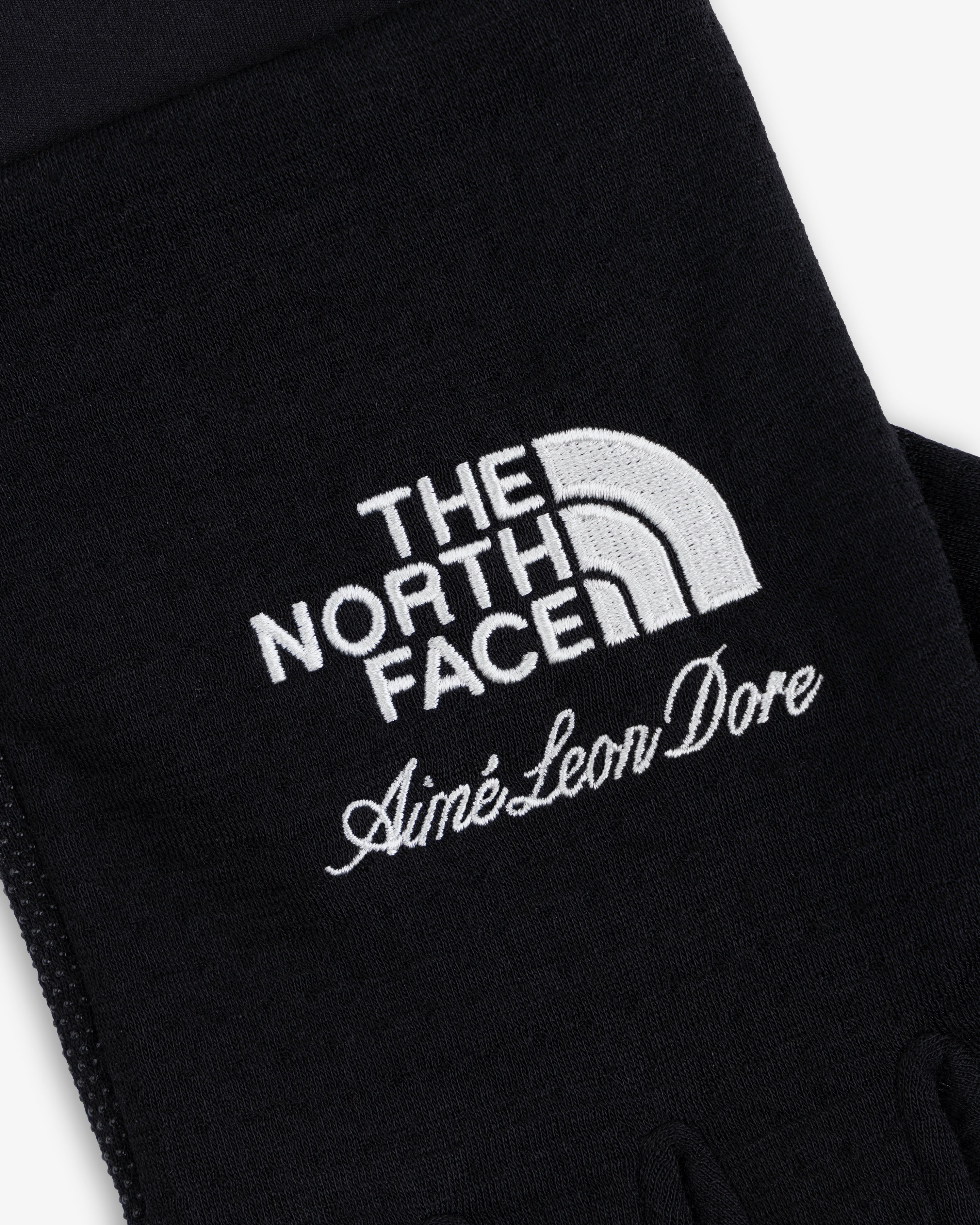 Close-up of ALD / The North Face DOTKNIT™ Liner Gloves with white embroidered logos on black fabric.