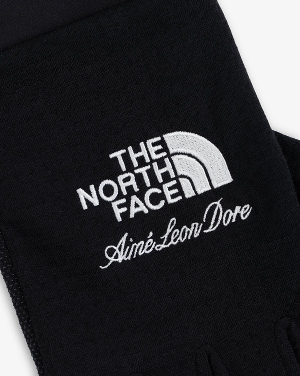 Close-up of ALD / The North Face DOTKNIT™ Liner Gloves with white embroidered logos on black fabric.