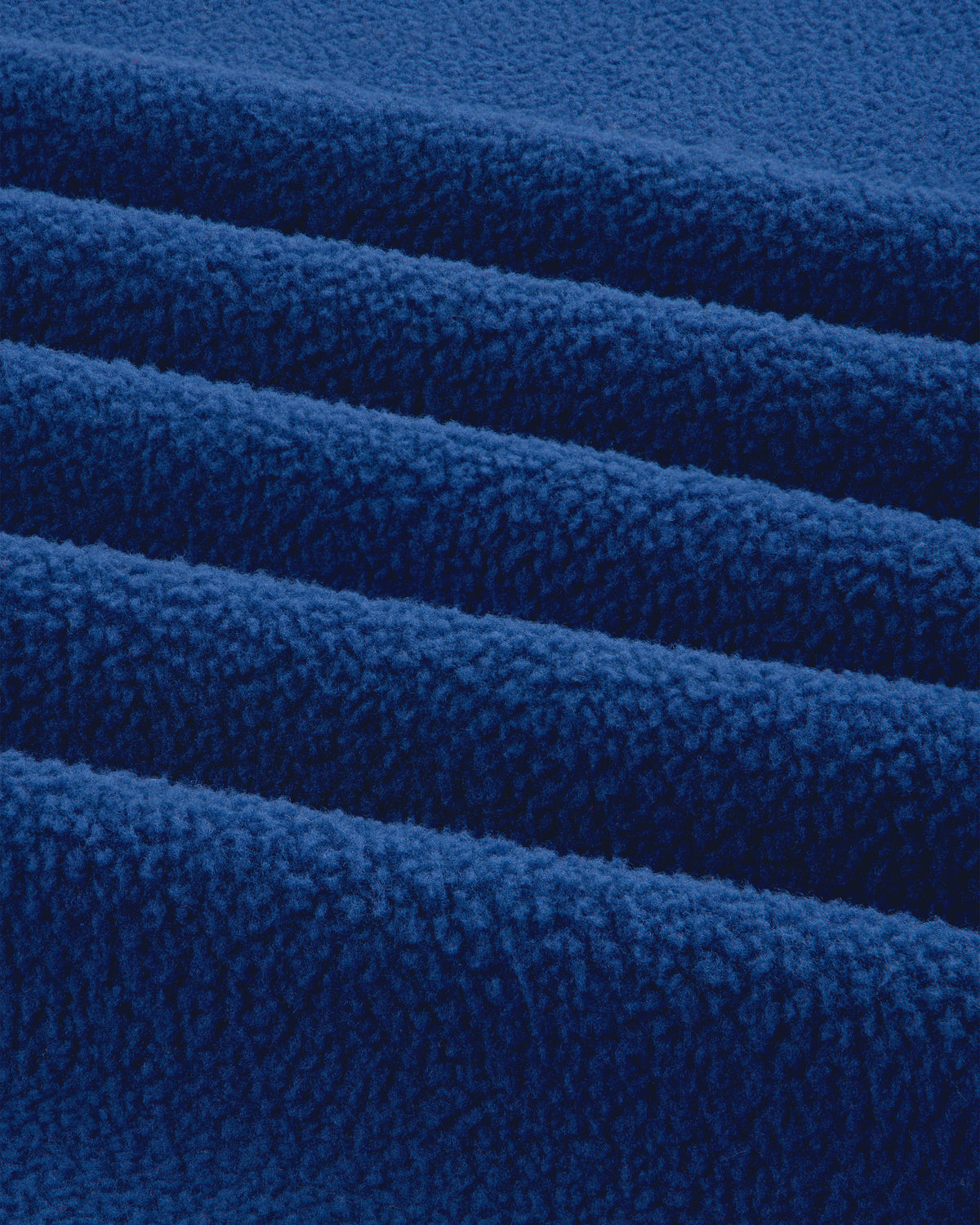 Close-up of folded ALD / The North Face Packable Fleece Blanket showing soft, textured blue fleece and parallel ridges.