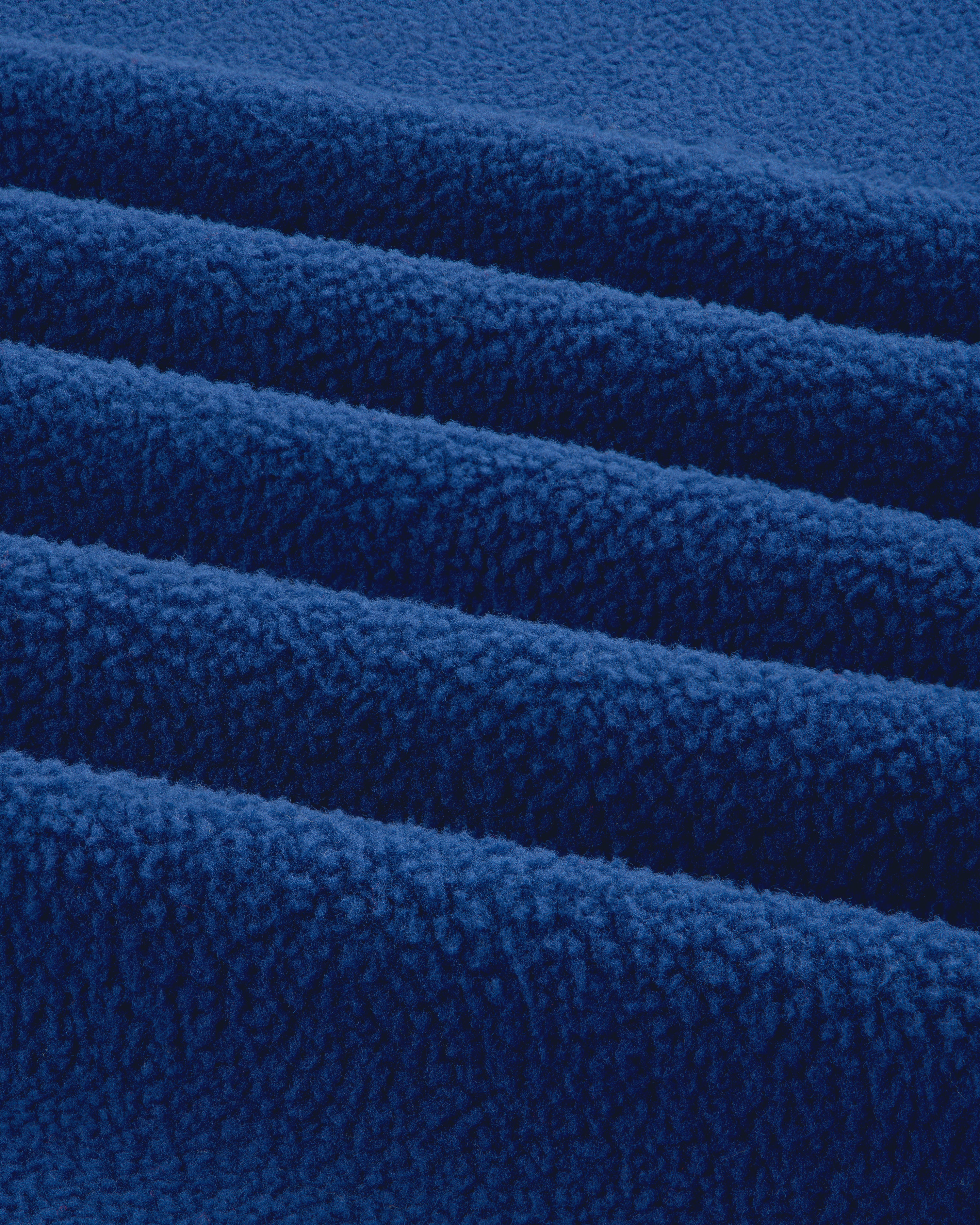 Close-up of folded ALD / The North Face Packable Fleece Blanket showing soft, textured blue fleece and parallel ridges.