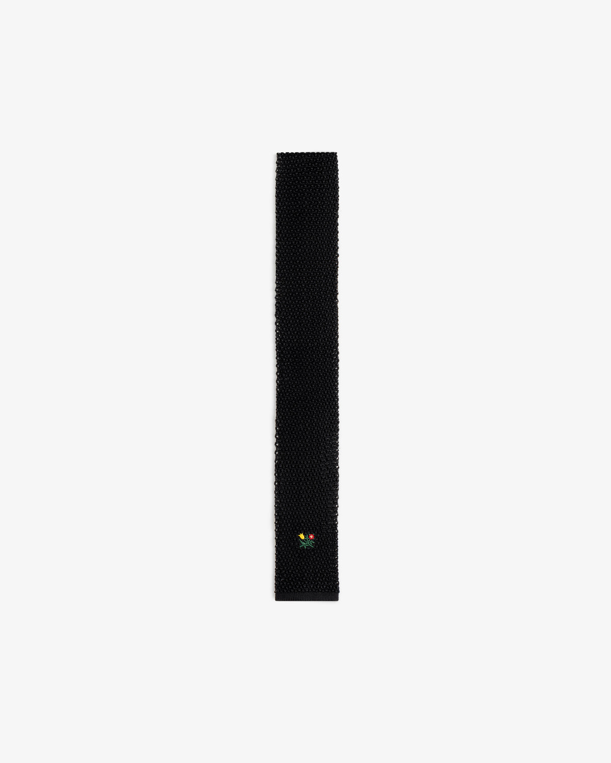 Crest Silk Knit Tie in black, featuring a small embroidered flower emblem near the tip.