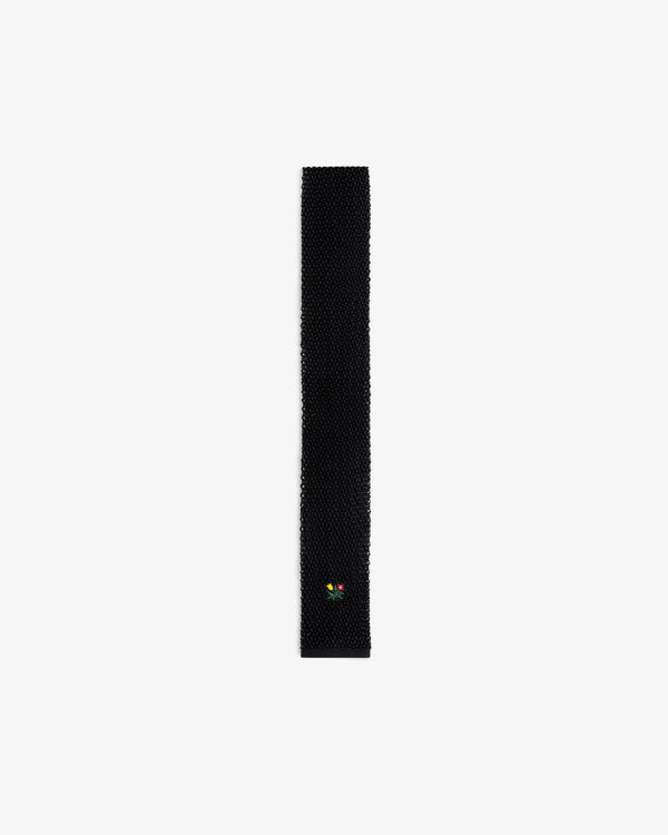 Crest Silk Knit Tie in black, featuring a small embroidered flower emblem near the tip.
