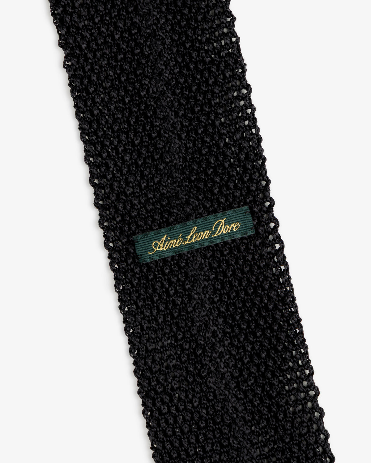 Crest Silk Knit Tie in black with a dark green fabric tag embroidered with gold text.